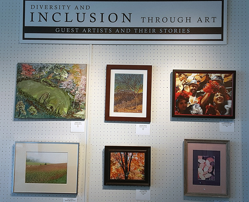Six pieces of art from the Passionate Focus 2023 exhibit are shown hanging beneath a sign that reads: Diversity and Inclusion through Art: Guests Artists and Their Stories