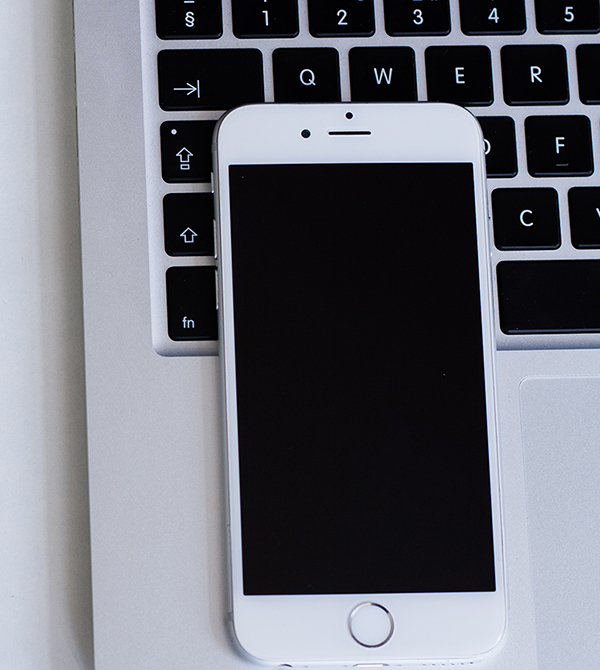 white iPhone with a blank screen laying on top of a white computer keyboard.